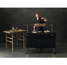 Man besprenkelt vleesspies op draaispitgrill met citroen, naast rustieke houten tafel