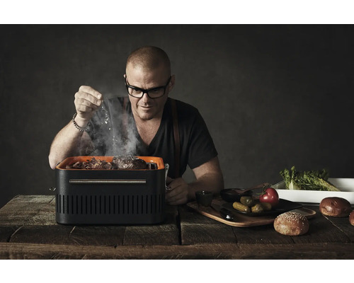 Man kruidt hamburgers op een draagbare grill, voedsel en ingrediënten op een houten tafel.