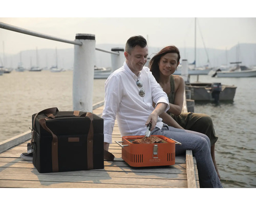 Scene met een draagbare grill, koeltas en twee mensen aan het water