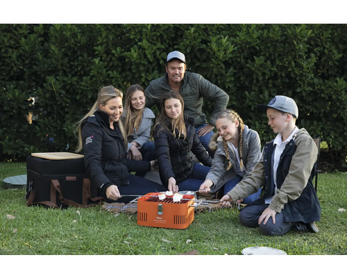 Familie die marshmallows grilt met een draagbare barbecue op een gazon.