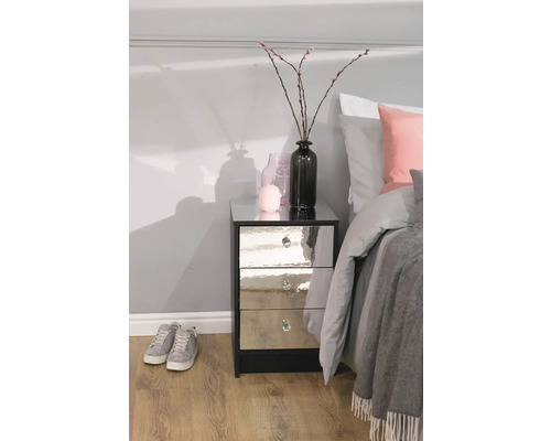 Nachtkastje met drie lades, spiegelende voorkanten en kristallen handgrepen in de slaapkamer naast een bed.