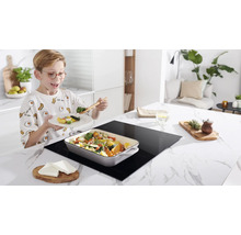 Jongen eet groenten van een inductiekookplaat in een keuken.