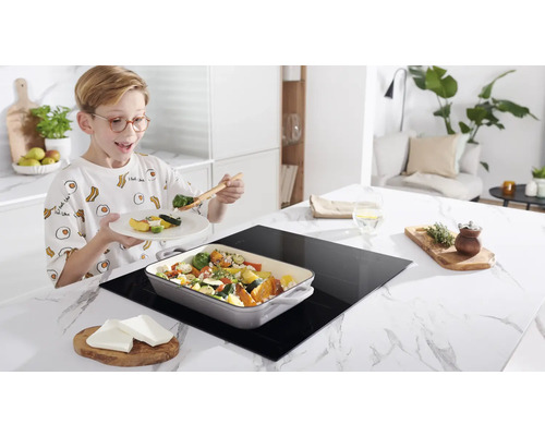 Jongen eet groenten van een inductiekookplaat in een keuken.