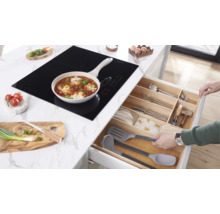 Kookscène met inductiekookplaat, pan met eten en open keukenlade met bestek