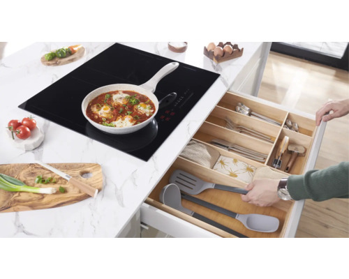 Kookscène met inductiekookplaat, pan met eten en open keukenlade met bestek