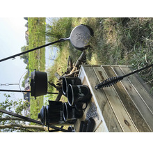 Kampvuur kookplaats met driepoot, pan, koffiepot, mokken en grillbestek op een houten tafel