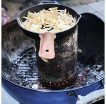Gietijzeren pan met uien op een aanmaakblokje in een houtskoolgrill