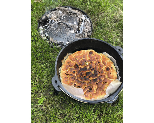 Brood in een Dutch oven met afgenomen deksel op gras.