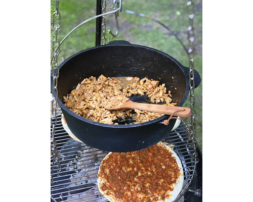 Goulashketel met voedsel en houten kooklepel boven grill
