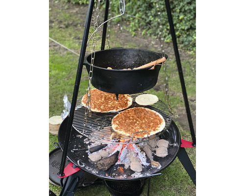 Barbecue met eten boven een open vuur en een pot die aan een driepoot hangt
