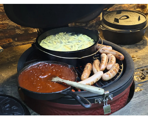 Op een grill bevinden zich een braadpan met saus, een pan met friet en meerdere worstjes.