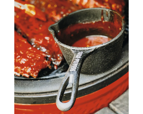 Gietijzeren pannetje met saus naast ribbetjes op de barbecue
