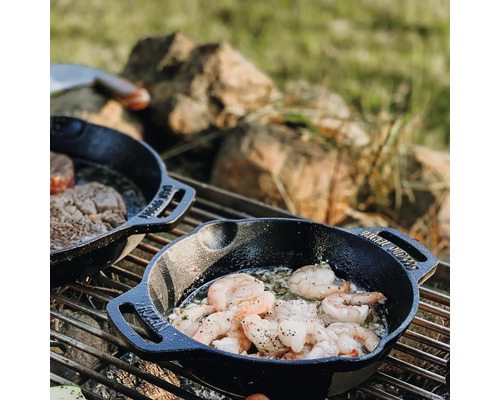Twee gietijzeren pannen met garnalen en biefstuk op een grill