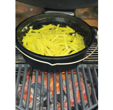 Een Dutch Oven staat op een grill boven gloeiende kolen, gevuld met frieten in olie.