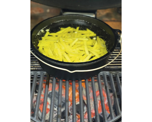 Een Dutch Oven staat op een grill boven gloeiende kolen, gevuld met frieten in olie.