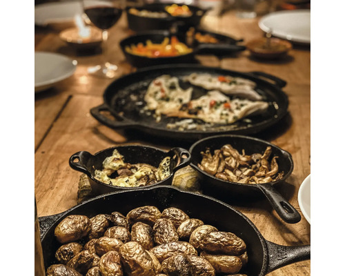 Houten tafel gedekt met eten in zwarte gietijzeren pannen