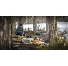 Bosscène met man, kampvuurplaats, driepoot met pot, stapel hout en kookgerei