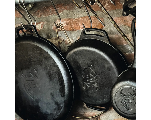 Verschillende gietijzeren pannen hangen aan haken voor een bakstenen muur.