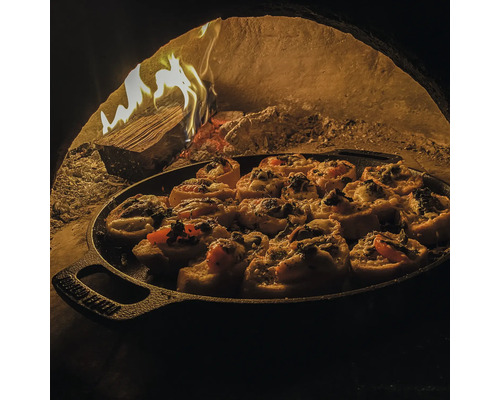 Pizza broodjes in een gietijzeren pan in een pizzaoven met houtvuur