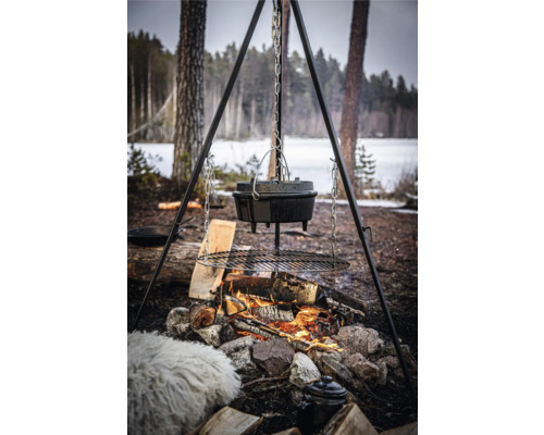 Bovenaanzicht van een Dutch oven boven een kampvuur op een driepoot met grillrooster in de buitenlucht.
