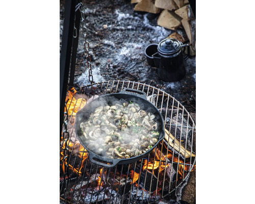 Paddenstoelen worden buiten bereid in een gietijzeren braadpan boven een kampvuur.
