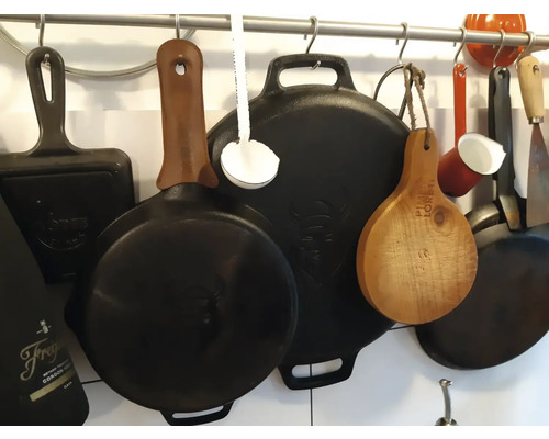 Diverse pannen en keukengerei hangen aan een stang.