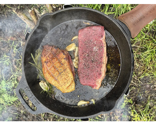Braadpan met biefstuk, eend, knoflook en rozemarijn op het fornuis