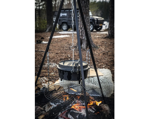 Een Dutch oven hangt aan een ketting boven een open vuur in de buitenlucht.