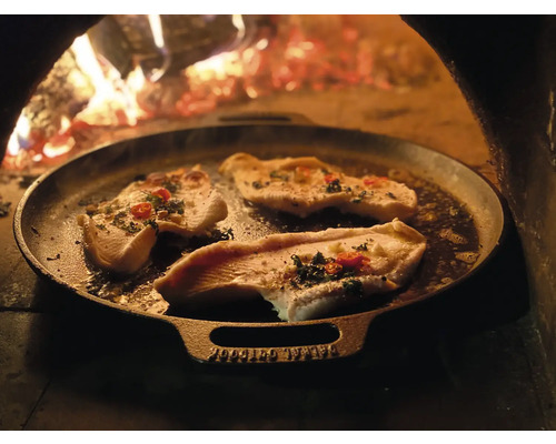 Visfilet wordt bereid in een gietijzeren pan voor een houtvuur