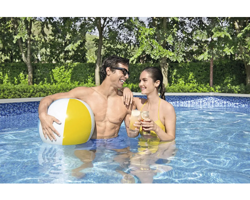 Een paar staat met een bal en drankjes in een zwembad.