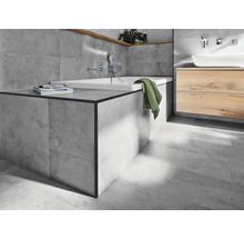 Lichte badkamer met ligbad, wastafel en grijze tegels.