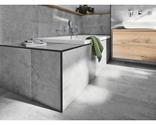 Lichte badkamer met ligbad, wastafel en grijze tegels.