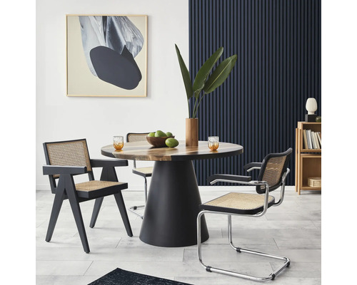 Eetkamer met ronde houten tafel, zwarte stoelframes en kunstwerk aan de muur.