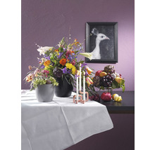 Decoratief stilleven met bloemstuk, fruitschaal, kaarsen en een ingelijste afbeelding van een witte pauw op een tafel met een wit tafelkleed.