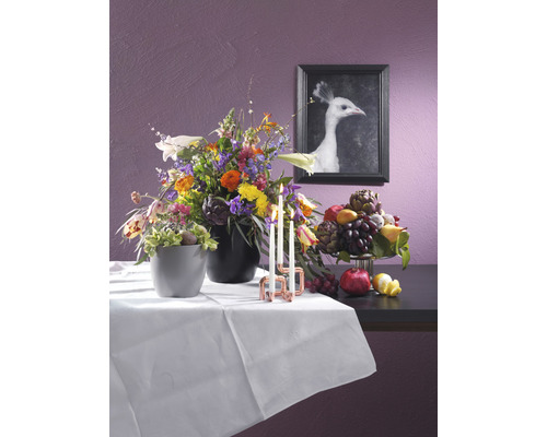 Decoratief stilleven met bloemstuk, fruitschaal, kaarsen en een ingelijste afbeelding van een witte pauw op een tafel met een wit tafelkleed.