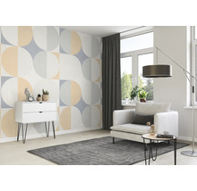 Woonkamer met geometrisch behang, fauteuil, tapijt en ladekast.