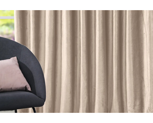 Beige gordijn naast een fauteuil met kussen.