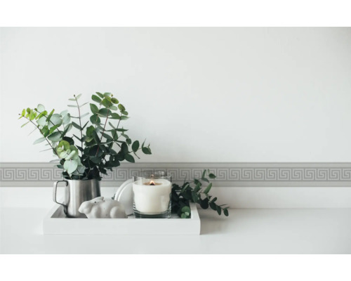 Decoratieve border met meandermotief op de muur boven een tafel met kaars en plant