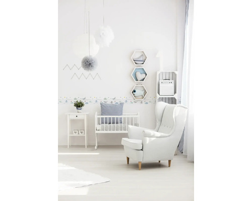 Licht ontworpen kinderkamer met babybed, fauteuil en decoratieve elementen.