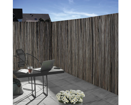 Schutting van natuurlijk materiaal naast een tuintafel met laptop buiten.