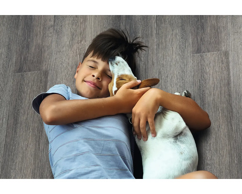 Een jongen ligt met een hond op een laminaatvloer.