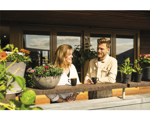 Een stel ontspant op het balkon met bloembakken en mokken.
