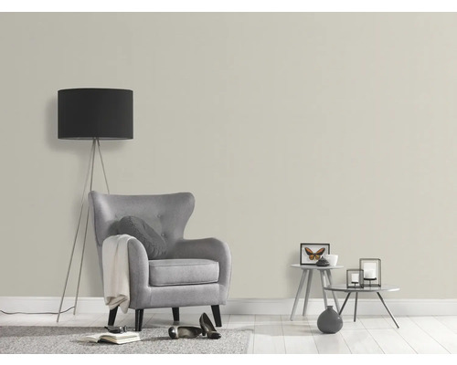 Woonkamer met fauteuil, vloerlamp en decoratieve tafels voor een lichte muur