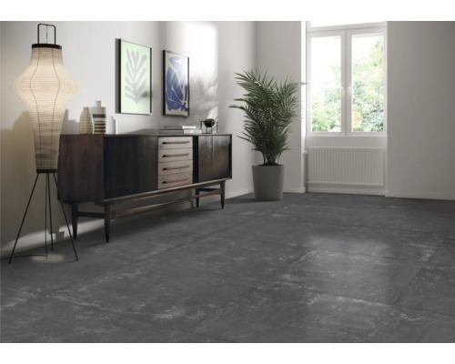 Woonkamer met donkere vloertegels, dressoir, staande lamp en kamerplant