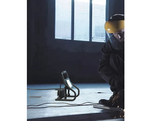 Arbeider met veiligheidsvizier slijpt met een bouwlamp voor verlichting.