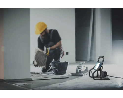 Tegelzetter aan het werk met emmer, tegelsnijder en bouwlamp