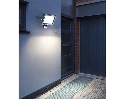 Buitenfoto van een verlichte LED-buitenlamp met bewegingsmelder aan een muur