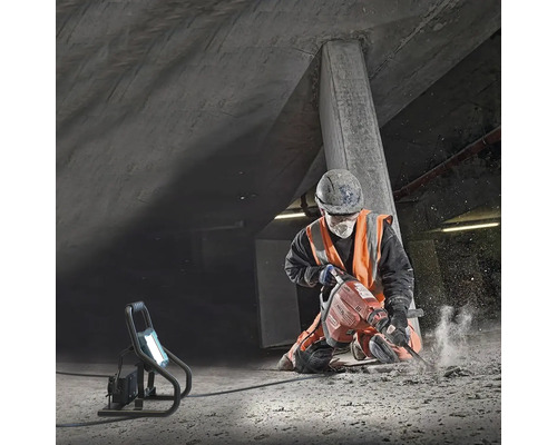 Een bouwvakker gebruikt een sloophamer in een betonnen put, verlicht door een bouwlamp.