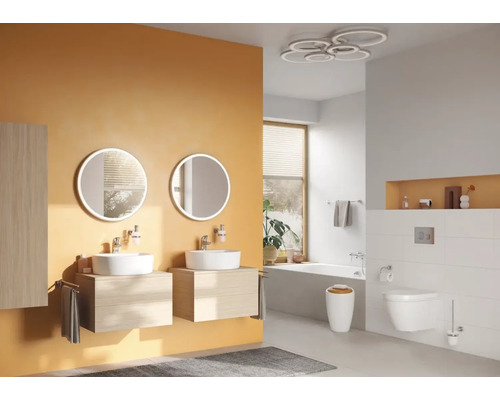 Badkamer met dubbele wastafel, ronde spiegels, bad en toilet.