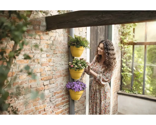 Vrouw bekijkt plantenbakken met bloemen op een muur.